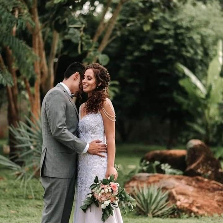 Noivos abraçados no jardim com pedras e palmeiras ao fundo